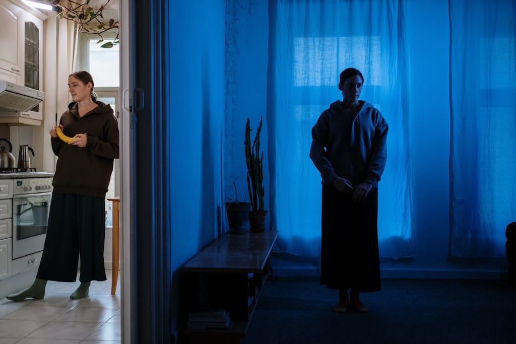 A woman stands in a dimly lit room facing contrasting environments, symbolizing inner duality.