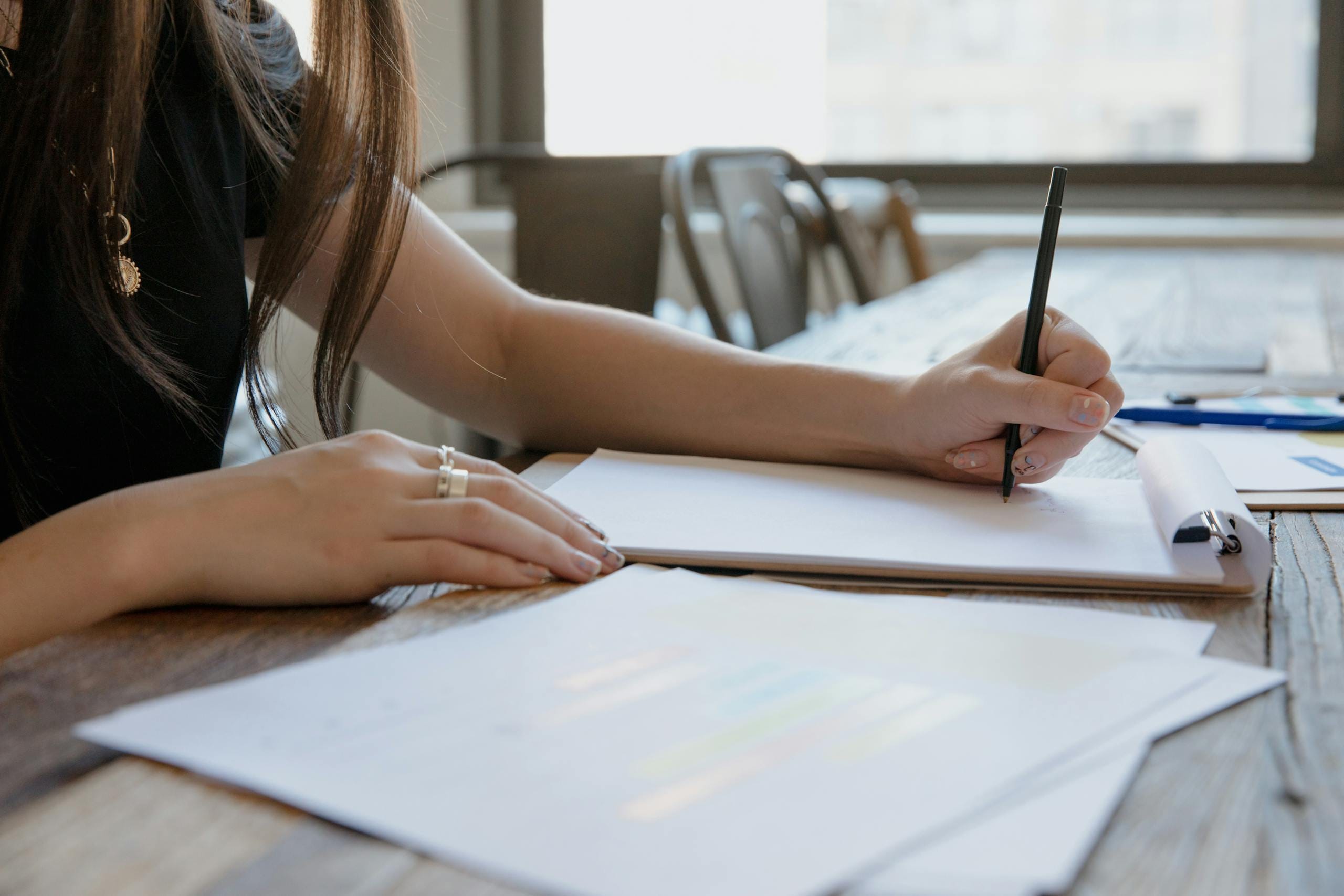 Close-up of a woman writing on paper at a wooden desk, indoors.