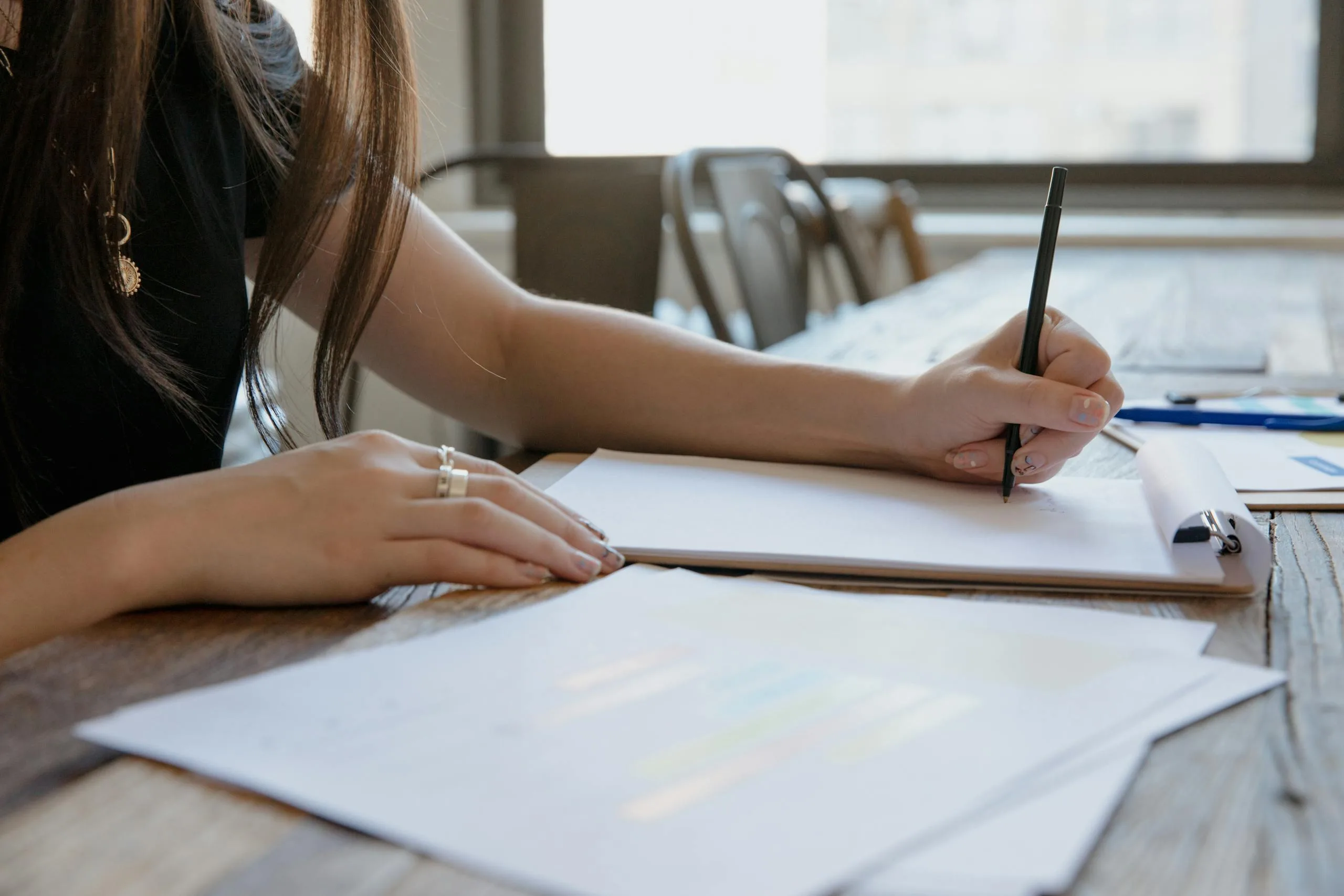 Close-up of a woman writing on paper at a wooden desk, indoors.